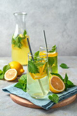 Two glasses of lemonade and a decanter on a gray background with lemons.