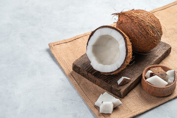 A whole and open coconut with pieces on a gray background.