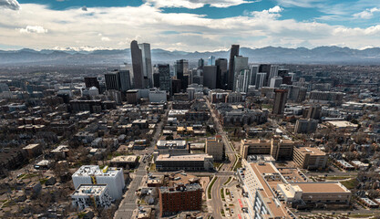 Aerial view of downtown Denver in Colorado. Several skyscrapers can be seen as well as mountains, clouds, and other smaller buildings. 