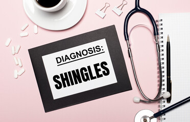 On a light pink background, a notebook with a pen, stethoscope, white pills, paper clips and a...