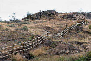 Fototapeta na wymiar Old log fence winds up a rocky and grassy hill