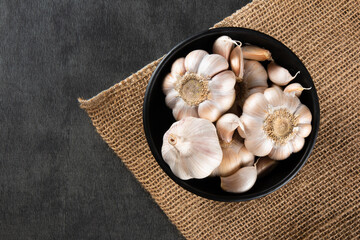 Garlic Cloves and Bulb in black bowl on jute and dark background