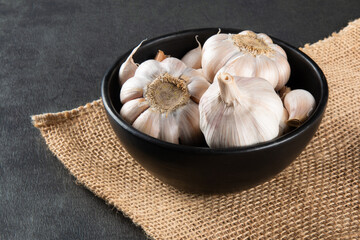 Garlic Cloves and Bulb in black bowl on jute and dark background