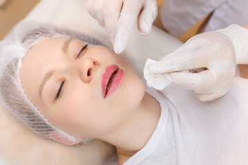 The beautician holds a drop of oil on her fingers after the injection of hyaluronic acid In front of the girl's lips