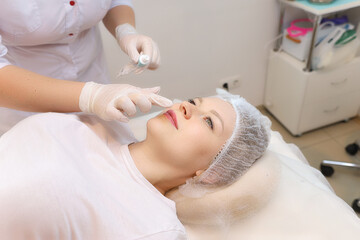 Obraz na płótnie Canvas The cosmetologist prepares the client's lips for the augmentation procedure