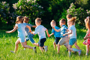 A group of happy children of boys and girls run in the Park on the grass on a Sunny summer day.