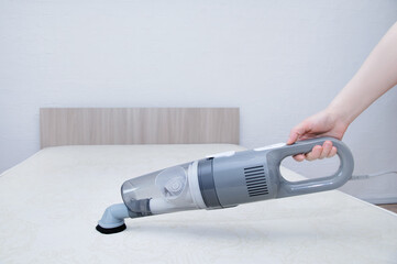 Vacuum the mattress of the bed. Handheld vacuum cleaner in the hand of Caucasian woman.