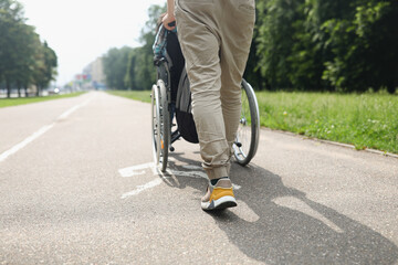 Man rolling wheelchair with disabled person on sidewalk closeup