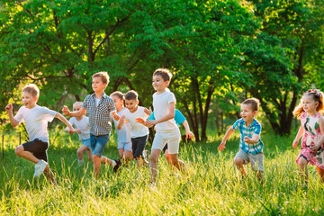 Obraz premium A group of happy children of boys and girls run in the Park on the grass on a Sunny summer day.