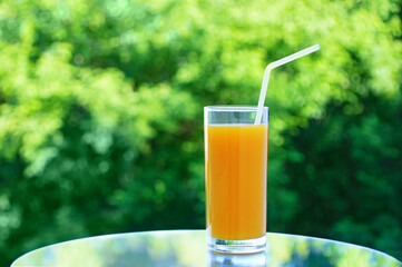 A glass of orange juice on a mirrored tabletop. Happy summer outdoors on  background of green foliage.