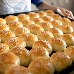 Fresh baked goods with sesame seeds. Hot crispy buns just out of oven. Rows of white round crispbreads or donuts are cooling. Soft focus. Close up shot.