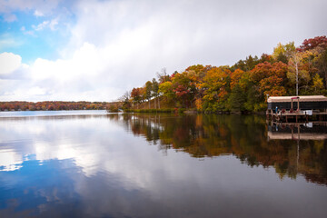 Fototapeta na wymiar The wind is calm on a Wisconsin lake in fall. The colors of the trees and the partly cloudy sky is reflected in the lake's surface.