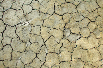 Dried brown clay surface covered with cracks. A bright, sunny day. Harsh shadows. Top view, textured, background.