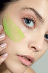 Young woman applying green gel face cream or facial mask at her face. Beauty model with perfect...