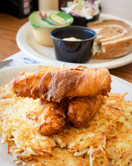 A traditional Wisconsin friday night fish fry from a diner including deep fried cod, coleslaw, marbled rye bread, applesauce, cola, tartar sauce and hash browns.