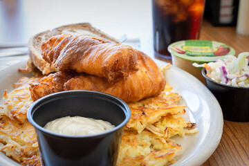 A traditional Wisconsin friday night fish fry from a diner including deep fried cod, coleslaw, marbled rye bread, applesauce, cola, tartar sauce and hashbrowns.