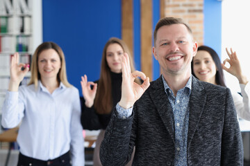 Businessman showing ok gesture on background of colleagues in office