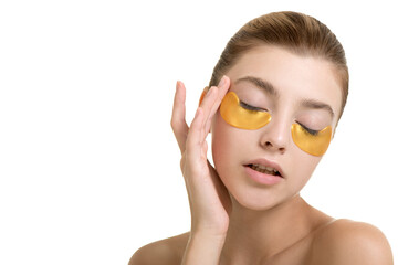 Beautiful young woman applies gold eye mask, isolated on white. Portrait of beauty model with natural nude make up cares about her skin. Spa, skincare and wellness