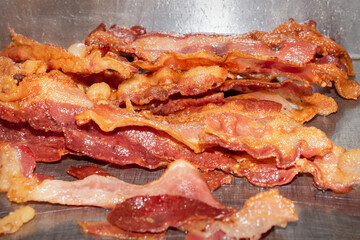A pile of bacon cooks on a flat grill in a restaurant.