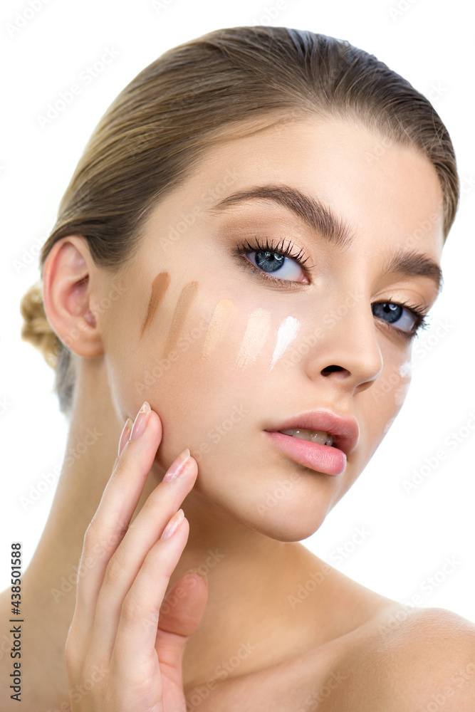 Wall mural young woman applying several color samples of facial foundation cream at her face.