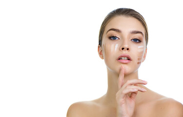 Young woman applying several color samples of facial foundation cream at her face.