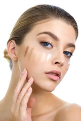 Young woman applying several color samples of facial foundation cream at her face.