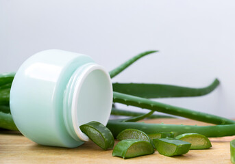 Sliced aloe vera leaves pouring out of the cosmetic jar, whole aloe leaves in the background. Natural cosmetics