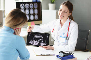 Woman obstetrician gynecologist showing patient photograph of ultrasound examination of fetus on digital tablet - obrazy, fototapety, plakaty