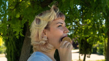 chica joven comiéndose un helado en el parque , chica de pelo corto y ojos claros con un helado en...