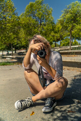 chica sentada en suelo haciendo una fotografía , mujer fotógrafa en el parque, chica joven haciendo una foto vertical con cámara réflex