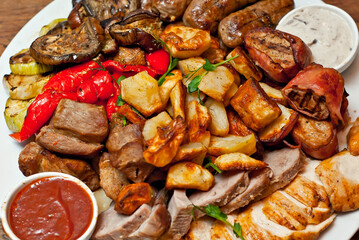 Assorted meat on a plate close up. Different types of meat and potatoes in a heap. Appetizer on a large plate with sauces.