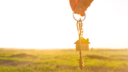 House key with keychain in hand. Background of sky, sunlight and field. Dream of home, building a...