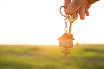 House key with keychain in hand. Background of sky, sunlight and field. Dream of home, building a...