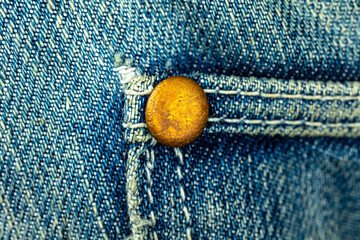 Bronze metal rivet on a blue denim jeans with stitched seam of pocket, close-up background