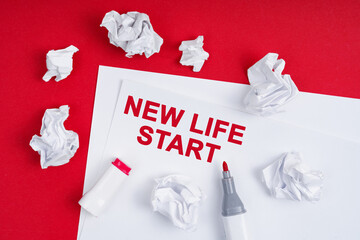 On a red background lies crumpled paper, a marker and a sheet of paper with the inscription - NEW LIFE START