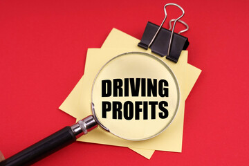 On a red background, a magnifying glass and a sticker with the inscription - Driving profits