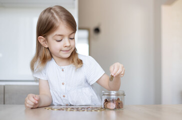 Obraz na płótnie Canvas Little girl putting coins into glass jar indoors. Money savings concept.