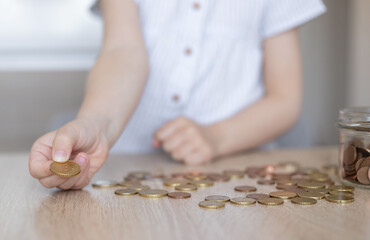 Kid hand putting money coins into clear jar, Child counting her saved coins, little girls hand holding coin, Child learning about saving for future.