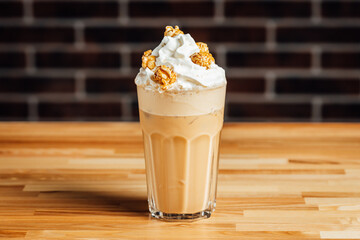 Iced coffee cafe latte with cream and caramel popcorn on bright table, coffe shop.