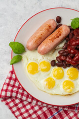 Top view of served English breakfast of fried eggs and sausages with red beans and tomato sauce