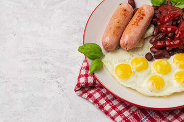 Horizontal photo of served English breakfast of fried eggs and sausages with red beans and tomato sauce with copy space