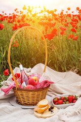 Fototapeta na wymiar Picnic on a poppy field at sunset. A wicker basket with wine, fruits and berries is on a blanket in a poppy field.