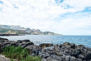 Fototapeta na wymiar View of the gulf of Giardini Naxos with solidified volcanic lava. Beauty in Sicily as a tourist attraction. Season on mediterranean sea. Ionian sea.