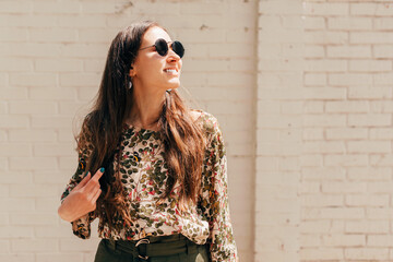 Fototapeta premium Portrait of a young cheerful woman smiling outside with sun glasses on looking away