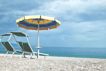 Two deck chairs and umbrella on pebble beach. Sicily as a tourist attraction. Season on mediterranean sea. Ionian sea.