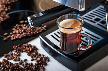 Transparent cup coffee close-up front view. Home coffee maker and process of making coffee drink. Defocus from coffee beans and copy space.