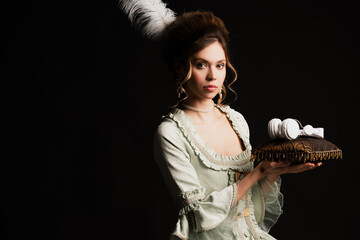 retro style woman in pastel grey dress holding velour pillow with wireless headphones isolated on black