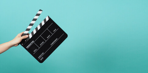 Hand is holding Black clapper board or movie clapperboard or slate on green mint or Tiffany Blue background.
