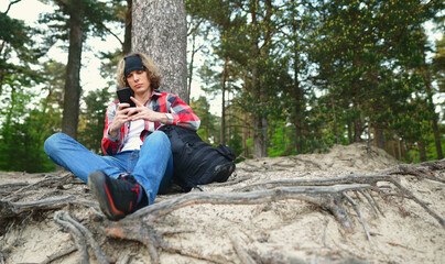 Male tourist with smartphone resting in the woods.