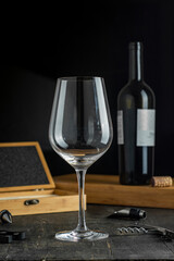 Empty wineglass on wooden table with accessories and black background.